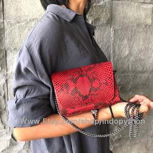 May include: A red snakeskin crossbody bag with a silver chain strap. The bag has a flap closure and a small zipper pocket on the front. www.Etsy.com/shop/indopython
