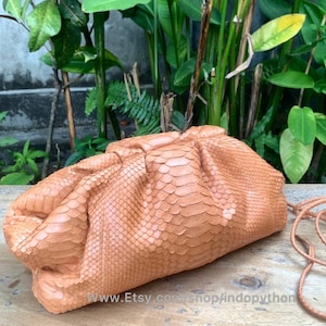 Może przedstawiać: Jasnobrązowa torebka typu kopertówka ze skóry pytona z sznurkowym zapięciem i długim paskiem. Torebka wykonana jest z prawdziwej skóry pytona i ma unikalny, fakturowany wzór.