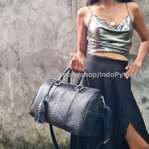 May include: A black leather handbag with a python skin pattern and a tassel. The bag has a top handle and a shoulder strap.