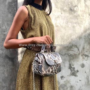 May include: A gold sleeveless dress with a black trim neckline and a snakeskin patterned handbag with a silver chain strap.