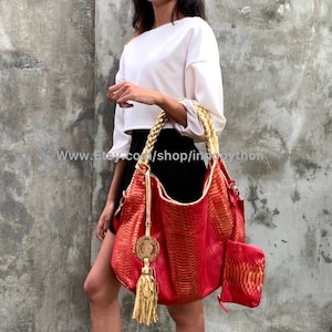 May include: A red and gold python leather handbag with a tassel. The bag has a braided gold rope handle and a small matching pouch.