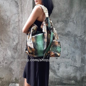 Op de afbeelding: Een groene en bruine slangleren handtas met een gevlochten band. De tas heeft een slouchy, hobo-stijl en is gemaakt van echt pythonleer.