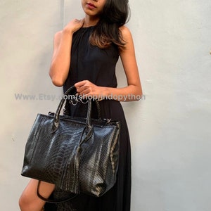 May include: A black snakeskin tote bag with a tassel. The bag has a top handle and a shoulder strap.