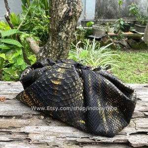 May include: A black and gold python skin clutch bag with a textured surface. The bag is folded and has a website address printed on it: www.Etsy.com/shop/indopython