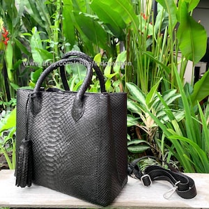 May include: Black leather handbag with a snakeskin pattern and a tassel. The bag has two top handles and a detachable shoulder strap.