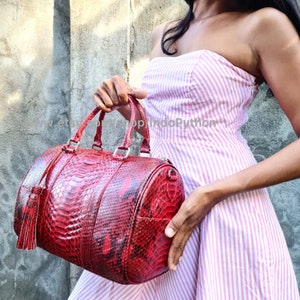 May include: A red python skin handbag with a tassel. The bag has a cylindrical shape and two top handles.