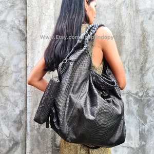 May include: A large black leather tote bag with a snakeskin pattern and braided leather handles. The bag is worn over the shoulder of a person wearing a gold top.
