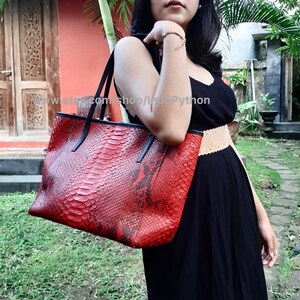 May include: A red and black tote bag made of python skin. The bag has a black leather handle and a black zipper closure.
