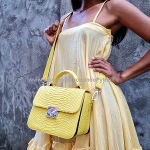 May include: A bright yellow python leather handbag with a top handle and a shoulder strap. The bag has a flap closure with a silver lock.