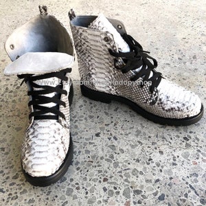 May include: A pair of white snake skin boots with black laces. The boots have a round toe and a chunky heel.