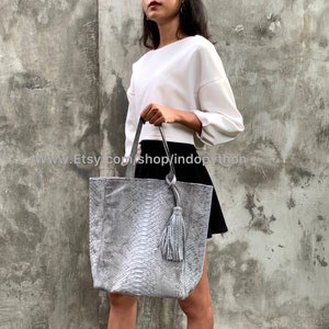 May include: A gray snakeskin tote bag with a tassel. The bag has a wide opening and a spacious interior. The bag is made of genuine leather and is perfect for everyday use.