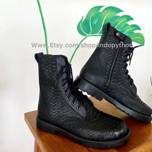 Könnte beinhalten: Zwei schwarze Lederstiefel mit Schlangenhautmuster und Schnürung. Die Stiefel haben einen Reißverschluss an der Seite und eine dicke Gummisohle.