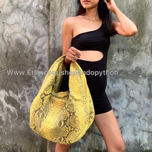 May include: A yellow python skin handbag with a slouchy, hobo style. The bag has a zipper closure and a single strap.