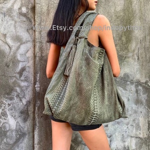 May include: A large, green, snakeskin-patterned leather tote bag with a tassel. The bag is worn over the shoulder of a person.