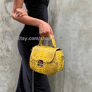 May include: A yellow snakeskin handbag with a silver chain strap. The bag has a flap closure with a silver lock.