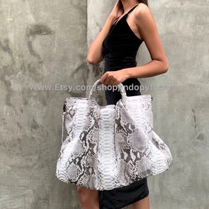 May include: A large, white and gray python skin tote bag with a structured, boxy shape. The bag has two top handles and a zipper closure.