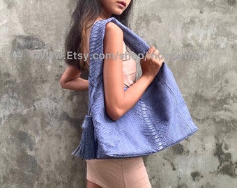 May include: A light blue snakeskin tote bag with a tassel. The bag has a textured surface and is worn over the shoulder.