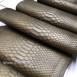 Op de afbeelding: Close-up van een stapel bruine python lederhuiden. Het leer heeft een getextureerd, schubbig oppervlak.