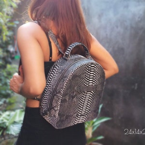 Könnte beinhalten: Ein runder Rucksack aus schwarzem und weißem Schlangenleder mit Reißverschluss. Der Rucksack misst 24x14x28cm.