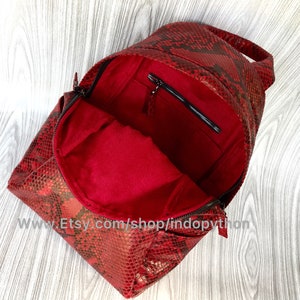 May include: Red snakeskin backpack with a zipped pocket on the inside. The backpack is open and the red lining is visible.