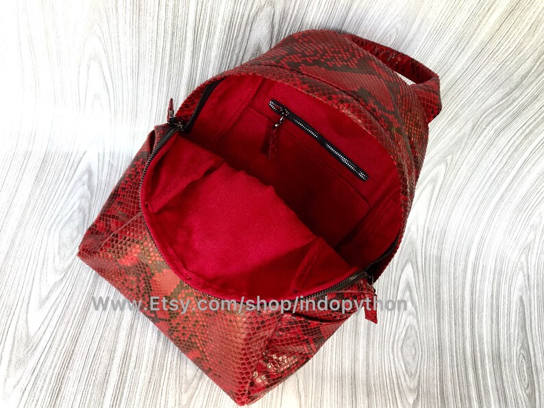May include: Red snakeskin backpack with a zipped pocket on the inside. The backpack is open and the red lining is visible.