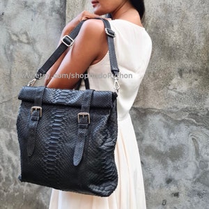 Peut inclure: Un sac cabas en cuir noir avec un motif peau de serpent et des boucles argent&eacute;es. Le sac a une longue bandouli&egrave;re r&eacute;glable et un rabat sup&eacute;rieur avec une fermeture &agrave; rabat.