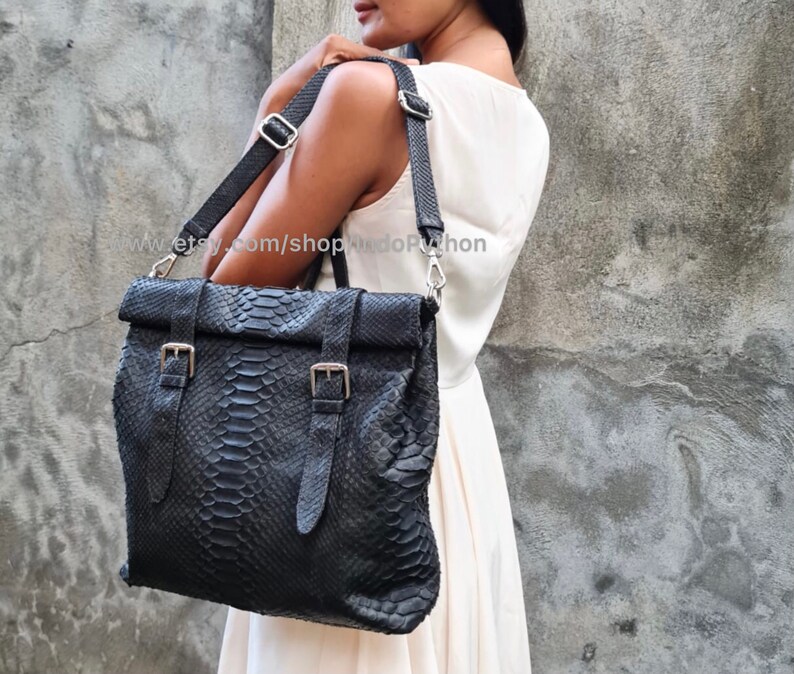 Peut inclure: Un sac cabas en cuir noir avec un motif peau de serpent et des boucles argent&eacute;es. Le sac a une longue bandouli&egrave;re r&eacute;glable et un rabat sup&eacute;rieur avec une fermeture &agrave; rabat.