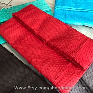 Peut inclure: Plusieurs pochettes colorées et texturées, rouges, turquoise, et noires. Les sacs présentent un motif en écailles, suggérant une peau de reptile. L'URL de la boutique Etsy est visible en bas de l'image.