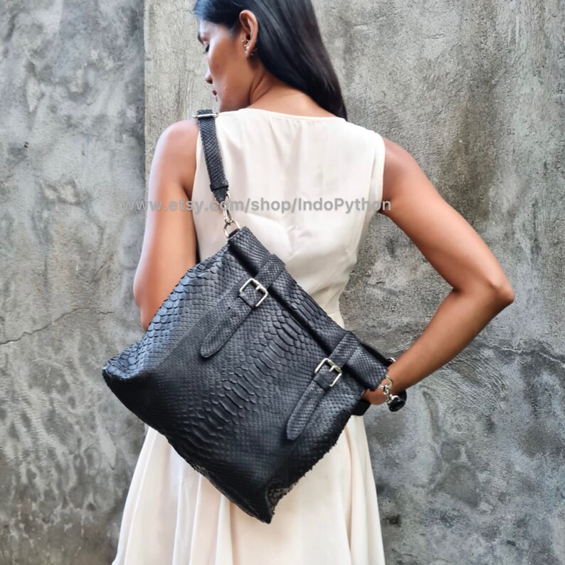 Peut inclure: Sac &agrave; bandouli&egrave;re en cuir noir avec un motif en peau de serpent et des boucles argent&eacute;es. Le sac a une longue bandouli&egrave;re et se porte sur l'&eacute;paule.