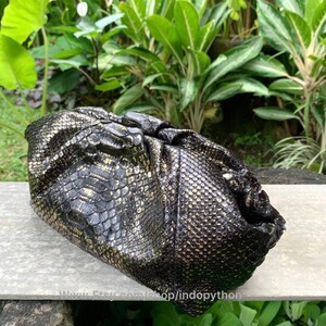 K&ouml;nnte beinhalten: Eine schwarze Clutch aus Pythonleder mit goldener Textur.