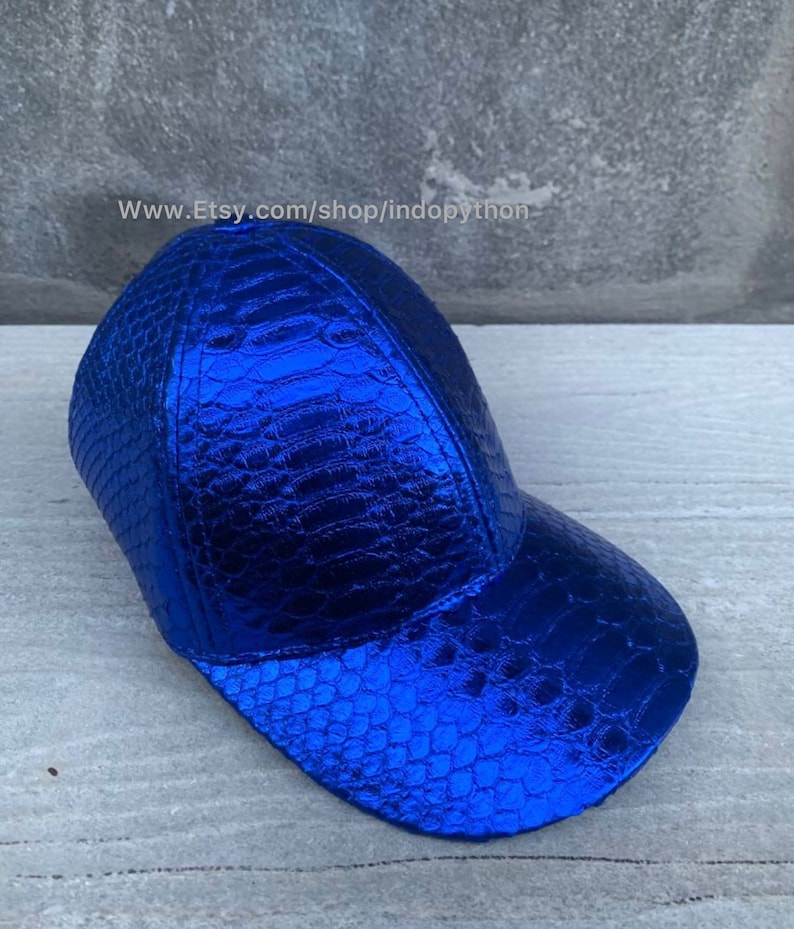 May include: A blue baseball cap with a crocodile-embossed leather design. The cap has a curved brim and a structured crown.