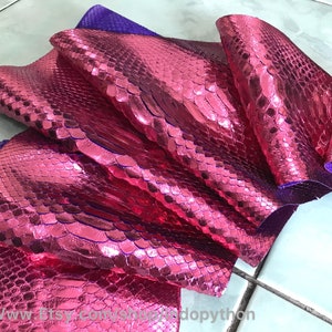 Puede incluir: Primer plano de una piel de serpiente rosa con brillo metálico. La piel está doblada y muestra la textura de las escamas. La piel es de un color rosa vibrante y tiene un ligero tono púrpura.