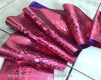 May include: A close-up of a pink snakeskin leather with a metallic sheen. The leather is folded and shows the texture of the scales. The leather is a vibrant pink color and has a slight purple hue.