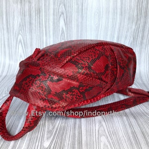 May include: A red snakeskin backpack with a single strap. The bag has a unique, woven design and a flap closure.