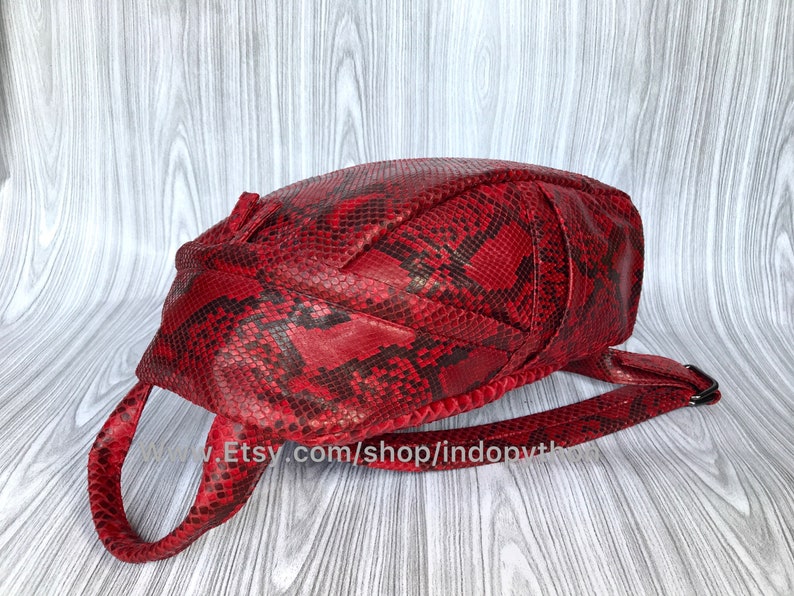 May include: A red snakeskin backpack with a single strap. The bag has a unique, woven design and a flap closure.
