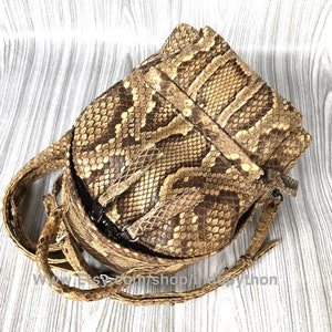 May include: A tan and brown snakeskin crossbody bag with a flap closure and adjustable strap. The bag features a textured pattern and a dark zipper. The strap is made of the same snakeskin material. The bag is designed to be worn over the shoulder.