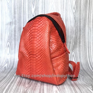 Pu&ograve; includere: Uno zaino arancione brillante in pelle di serpente con una cerniera nera e spalline regolabili. Lo zaino &egrave; realizzato in vera pelle di pitone.