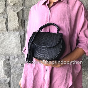 May include: A black leather handbag with a snakeskin pattern and a tassel. The bag has a top handle and a flap closure.