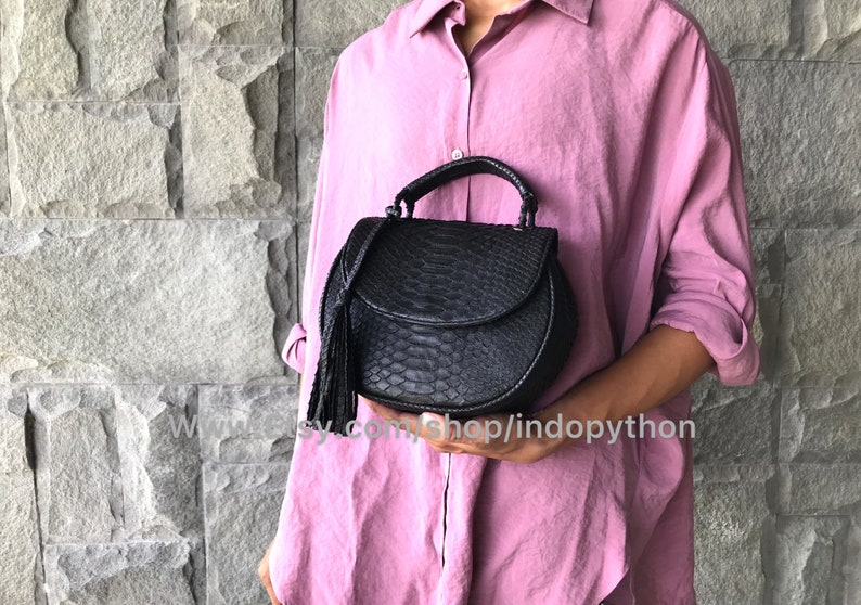 May include: A black leather handbag with a snakeskin pattern and a tassel. The bag has a top handle and a flap closure.