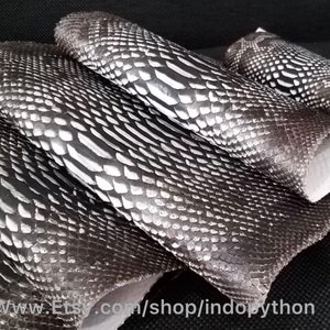 Może przedstawiać: Zbliżenie na stos czarnej i srebrnej sk&oacute;ry pytona. Sk&oacute;ra ma fakturowany, łuskowaty wz&oacute;r.