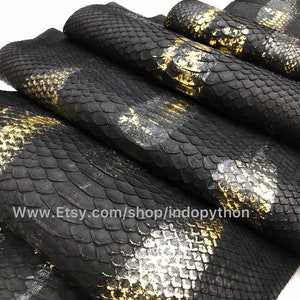 Op de afbeelding: Close-up van zwart pythonleer met gouden accenten. Het leer is in een stapel gelegd, waardoor de textuur en het patroon van de schubben zichtbaar zijn. Het websiteadres "www.Etsy.com/shop/indopython" is zichtbaar in de afbeelding.