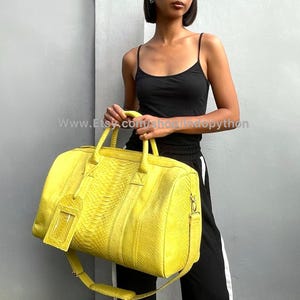 May include: A bright yellow python leather duffel bag with a top handle and a long shoulder strap. The bag has a small pocket on the front.