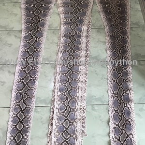 May include: Three long strips of light gray python skin with a dark gray pattern. The skin is laid out flat on a tiled floor.