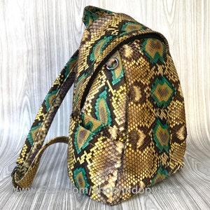 Peut inclure: Un sac &agrave; dos en cuir de serpent brun, vert et jaune avec une fermeture &agrave; glissi&egrave;re. Le sac &agrave; dos a une seule sangle et une petite poche sur le devant.