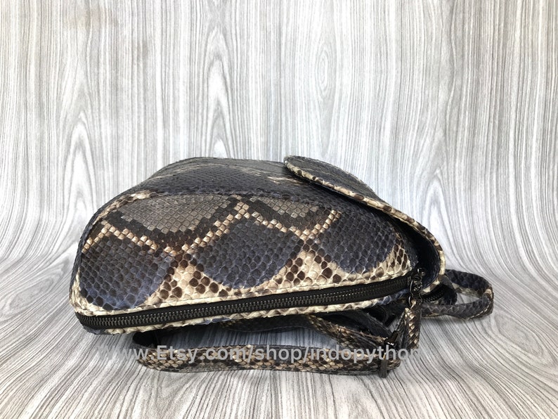 Pu&ograve; includere: Una borsa a mano in pelle di pitone vera, di colore marrone e nero, con chiusura a zip e una lunga tracolla.