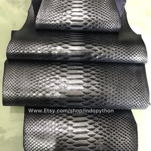 May include: Four pieces of black python leather, stacked on top of each other. The leather has a textured, scaly pattern. The website address www.Etsy.com/shop/indopython is printed on the bottom piece of leather.