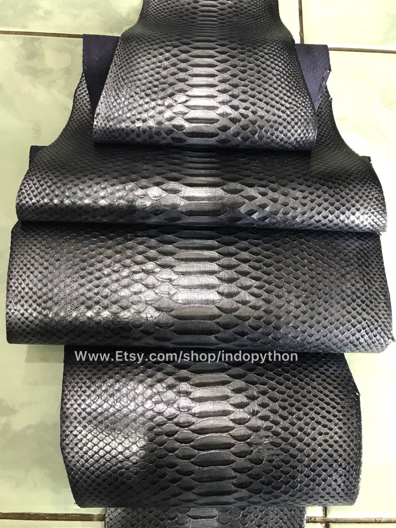 May include: Four pieces of black python leather, stacked on top of each other. The leather has a textured, scaly pattern. The website address www.Etsy.com/shop/indopython is printed on the bottom piece of leather.