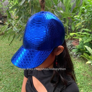 May include: A blue baseball cap made of snakeskin with a shiny, metallic finish. The cap has a curved brim and a structured crown.