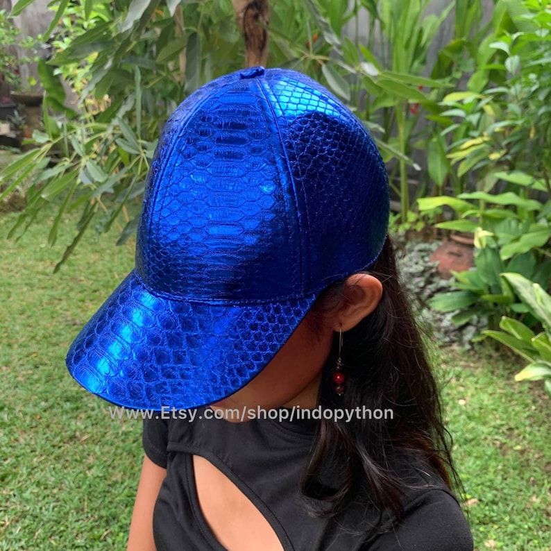 May include: A blue baseball cap made of snakeskin with a shiny, metallic finish. The cap has a curved brim and a structured crown.