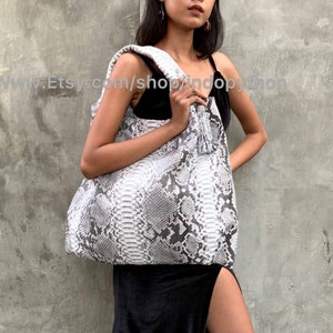 May include: A white and gray snakeskin tote bag with a tassel. The bag has a slouchy, casual style and is made of genuine leather.